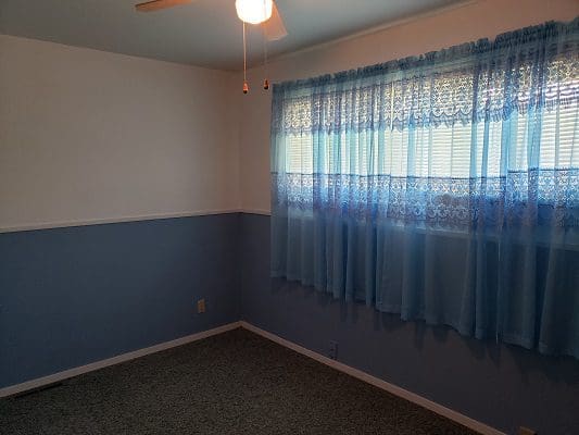 An empty room with blue curtains and a fan.