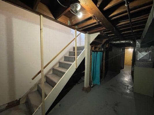 An empty basement with stairs and a ladder.