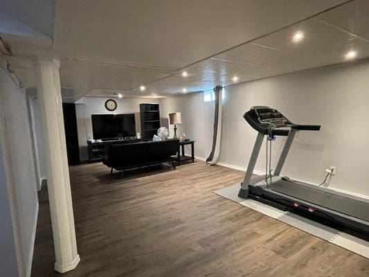 A basement with a treadmill and a tv.
