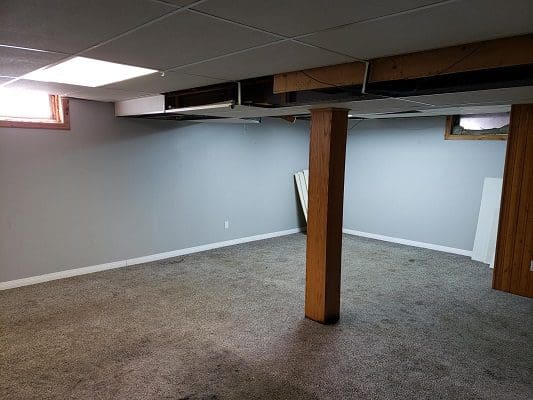 An empty basement with a ceiling fan and carpet.