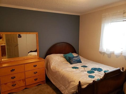 A bedroom with a bed, dresser and mirror.