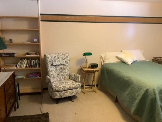 A small bedroom with a bed, chair and bookshelf.