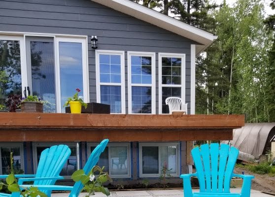 Two blue adirondack chairs in front of a house.