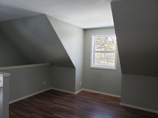 An empty attic room with hardwood floors and a window.