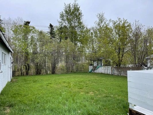A backyard with grass and a white fence.