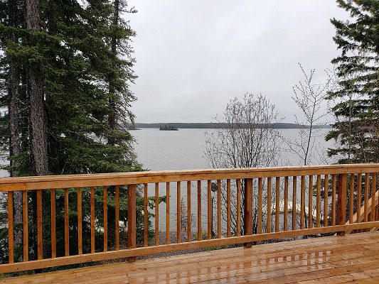 A deck with a view of a lake and woods.