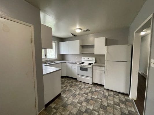 An empty kitchen with white cabinets and a stove.