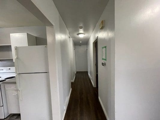 A hallway with a white refrigerator and wood floors.