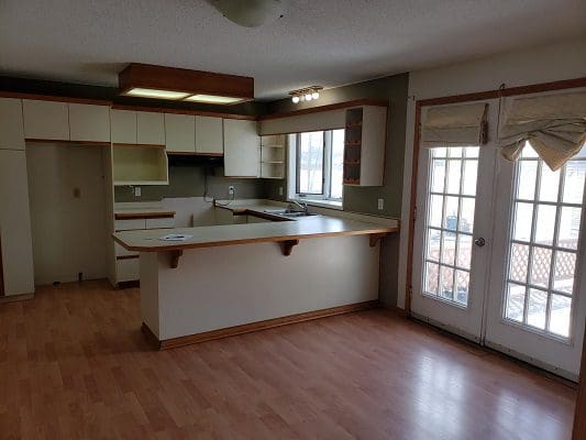 An empty kitchen with hardwood floors and a sliding glass door.