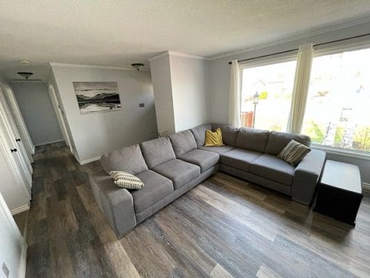 A living room with a grey couch and hardwood floors.