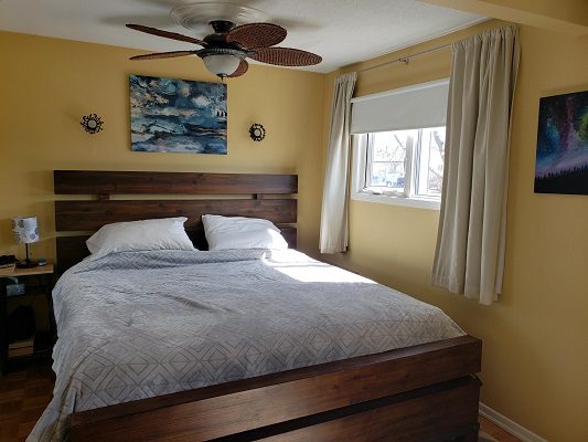 A bed in a bedroom with yellow walls and a ceiling fan.