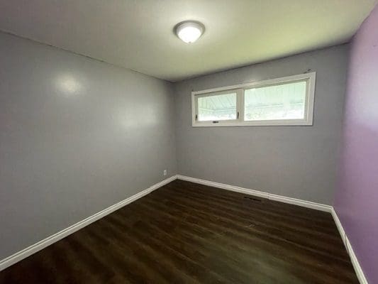 An empty room with purple walls and hardwood floors.