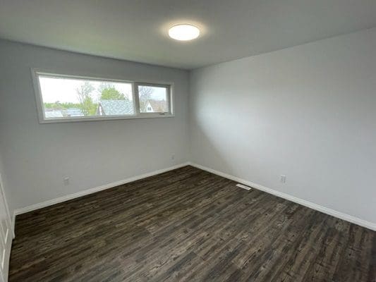 An empty room with wood floors and a window.