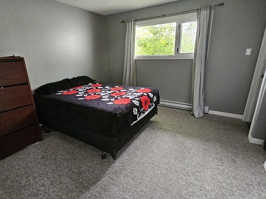 A bedroom with a bed, dresser and a window.