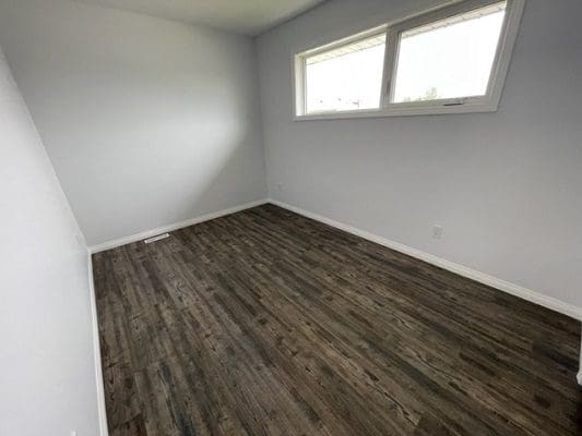 An empty room with wood floors and a window.