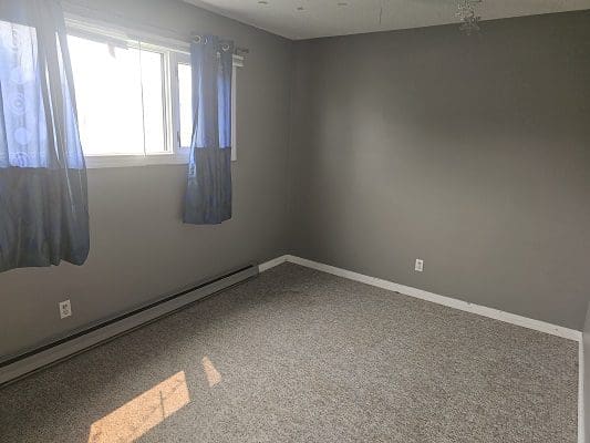 An empty room with gray walls and blue curtains.