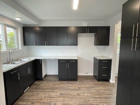 An empty kitchen with black cabinets and hardwood floors.