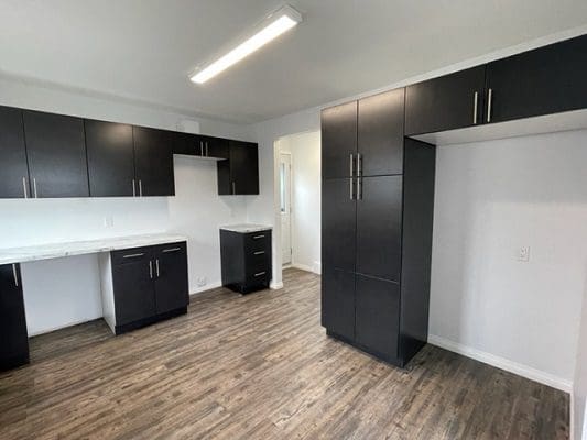 An empty kitchen with black cabinets and hardwood floors.