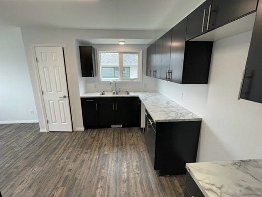 An empty kitchen with black cabinets and hardwood floors.