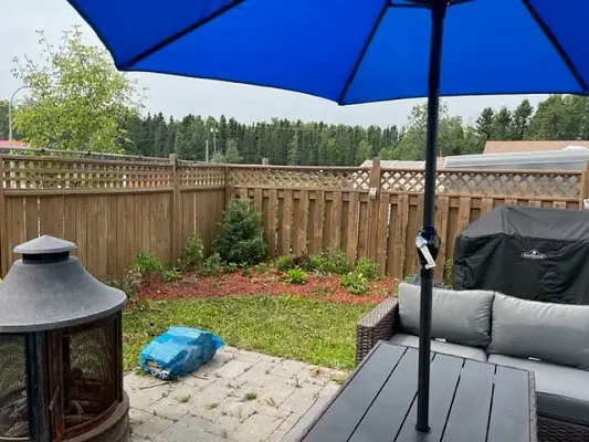 A backyard with a blue umbrella and a fire pit.