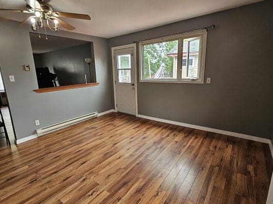 Empty living room with hardwood floors and a ceiling fan.