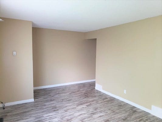 An empty living room with hardwood floors and a beige wall.