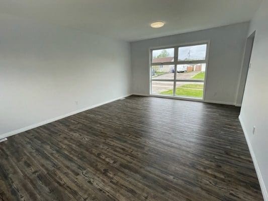 An empty room with hardwood floors and a window.