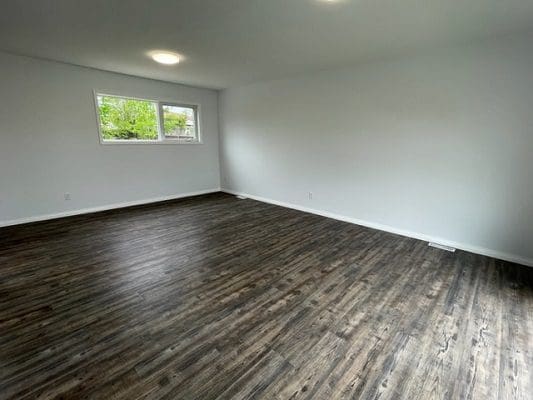 An empty room with wood floors and a window.