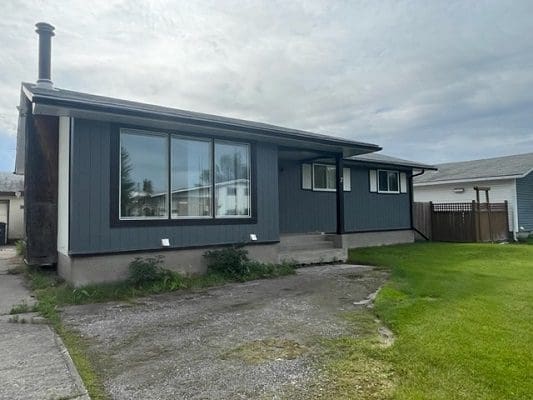 Gray house with large windows and lawn.