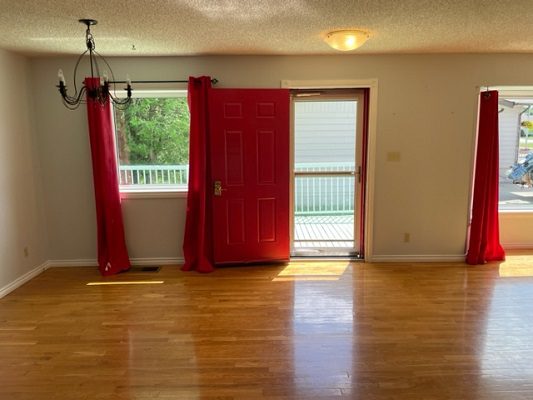 Empty living room with red curtains and hardwood floors.