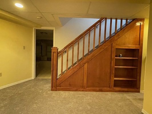 A basement with stairs and a bookcase.