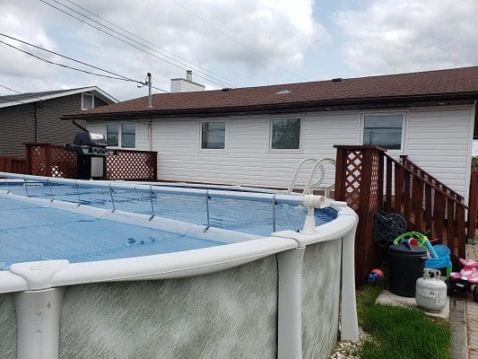 Above-ground pool behind house with grill.