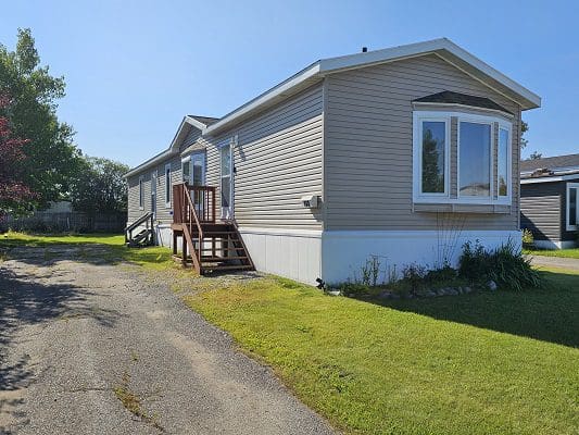 Beige mobile home with steps and lawn.