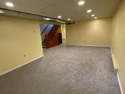 Empty basement with stairs and carpet.