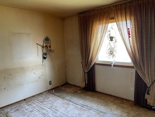 Damaged room with wall hangings and curtains.
