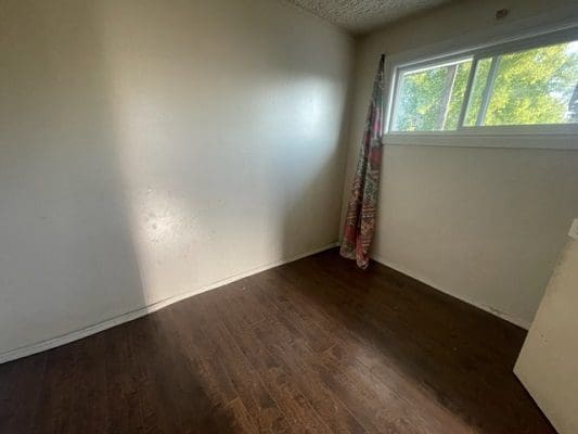 Empty bedroom with wood floor and window.