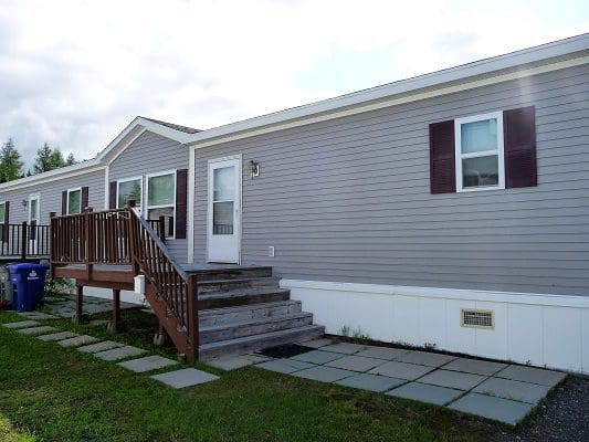 Gray mobile home with wooden deck.