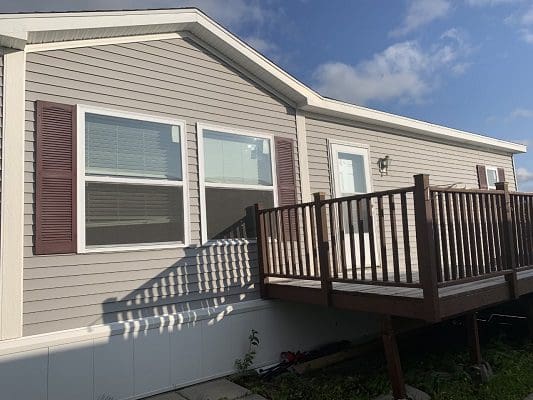 Tan mobile home with deck and shutters.