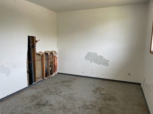 Damaged room with exposed pipes and wall.