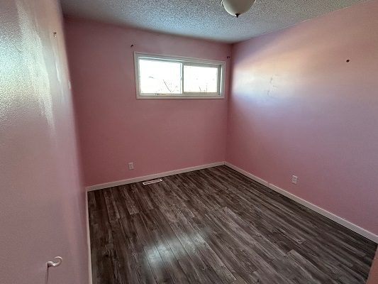 A pink room with hardwood floors and a window.