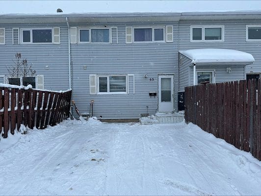 Snow-covered duplex house with fenced yard.