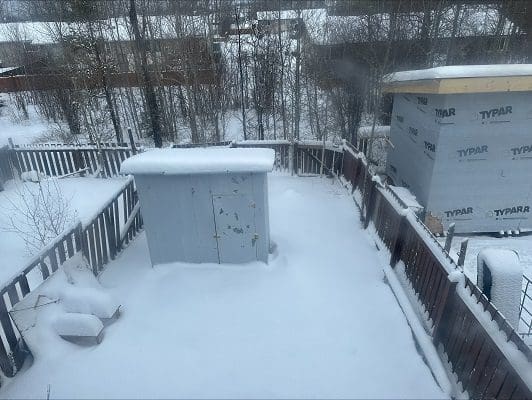 Snowy backyard with shed and fence.