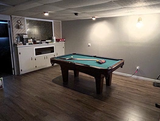 Basement pool table with cue and balls.