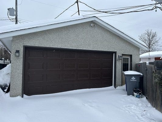 Snow-covered garage with brown door.