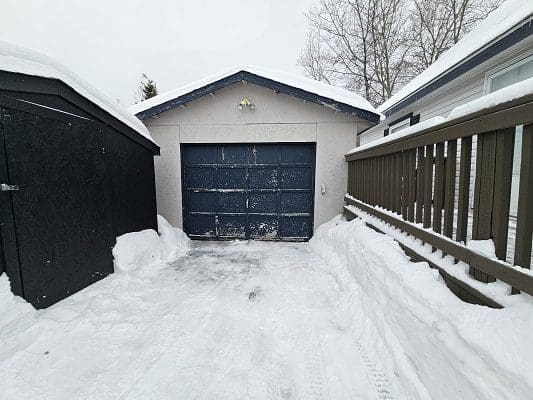 Snowy driveway with garage and shed.