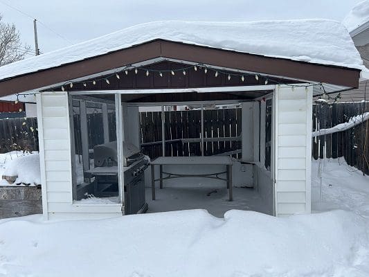 Snow-covered gazebo with grill and table.