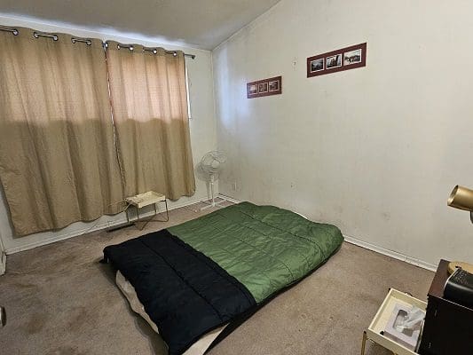 Bedroom with bed, curtains, and small table.