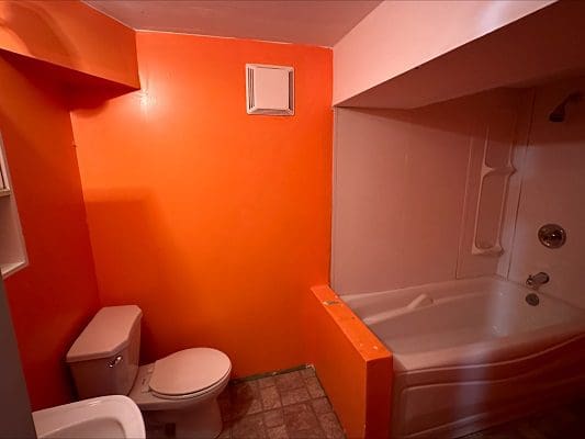 Orange bathroom with toilet and tub.