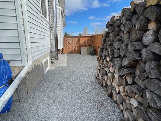 Gravel pathway, house, and woodpile.