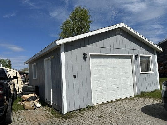 Gray detached garage with white door.